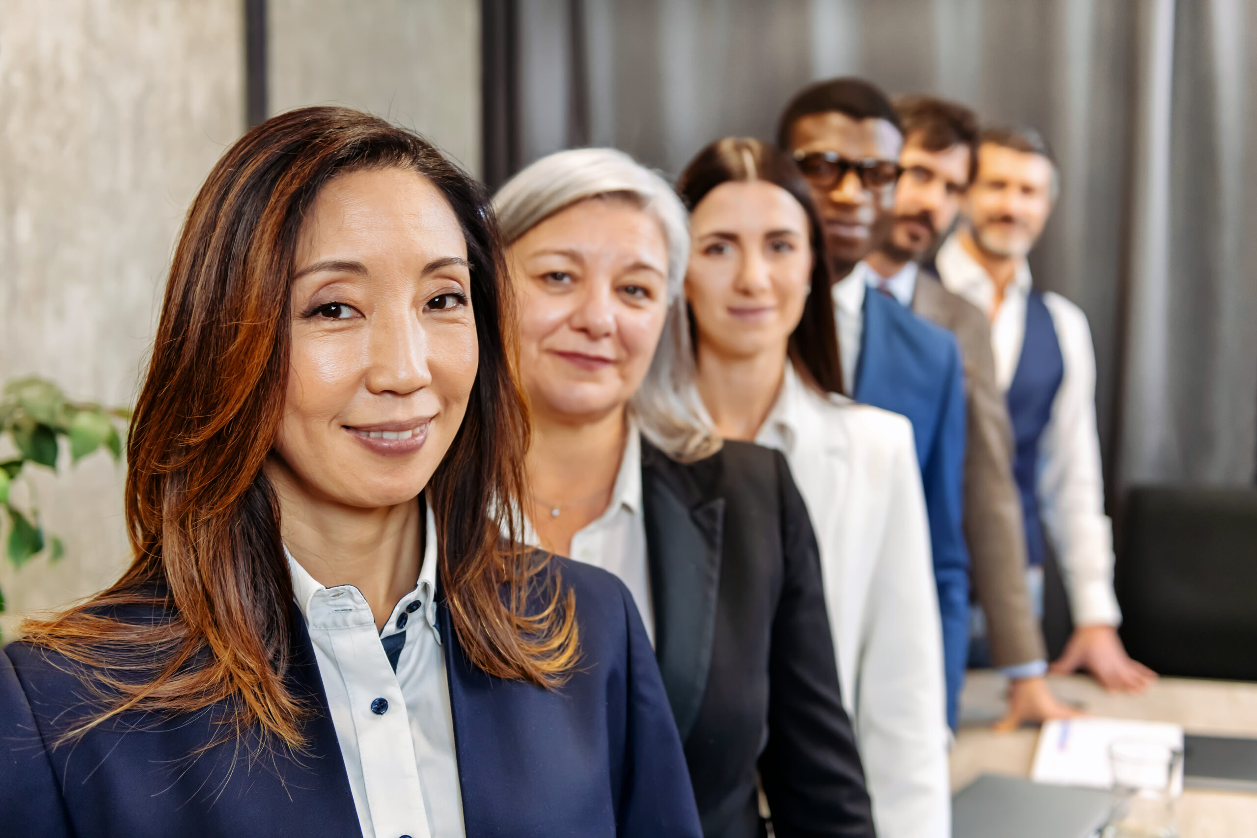 Team of diverse colleagues in formal wear standing in row and looking at camera in modern office